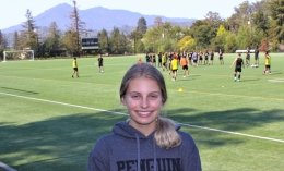 Photo of Abbie Gould in dark gray ֱ soccer hoodie standing at Kennelly Field with men's soccer practice and Mt. Tam in background 