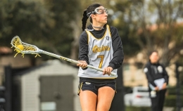 Photo of ֱ women's lacrosse player Taylor Pieri, wearing white number 7 jersey, looking downfield left while holding her lacrosse stick with both hands angled to her right.