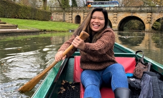Photo of ֱ Scholar Christina Pathoumthong smiling while sitting in a boat rowing in canal through the University of Oxford campus 