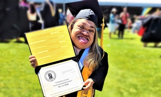 Photo of Patricia Ramos '22, in black cap and gown, posing holding her diploma she received at ֱ Commencement in May 2022